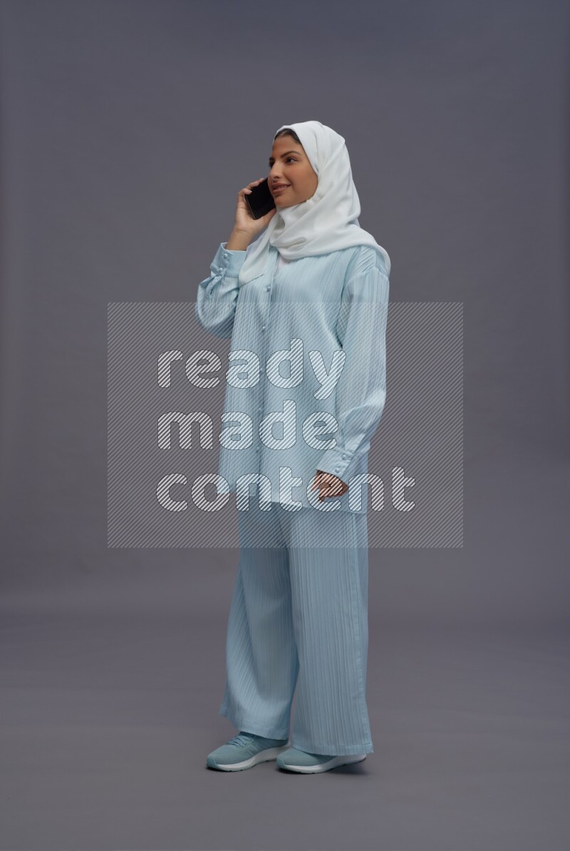Saudi woman wearing hijab clothes standing talking on phone on gray background