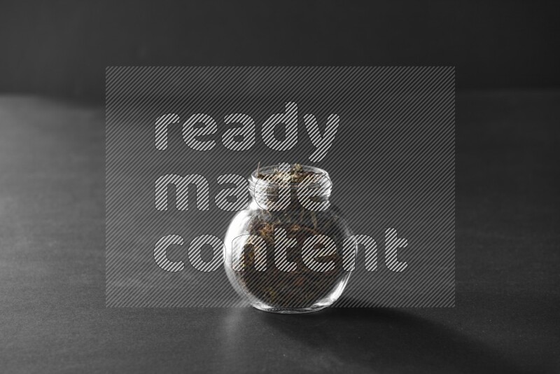 A glass spice jar full of basil on black flooring