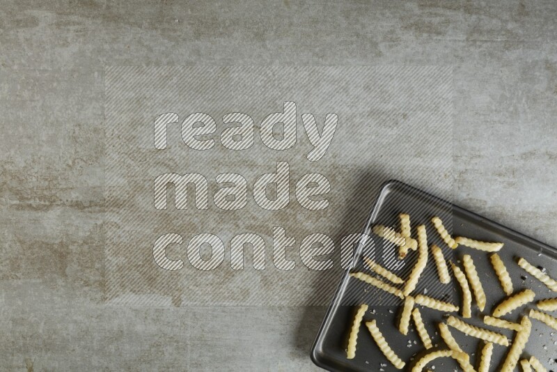 crinkle fries in a black stainless steel rectangle tray on grey textured counter top