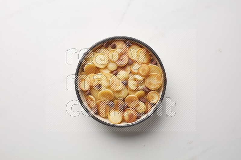 Top-view shot of chocolate chips cereal pancakes in a round bowl on white background
