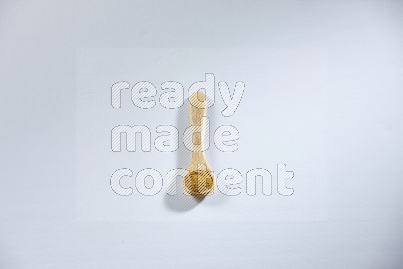 A wooden spoon full of turmeric powder on white flooring