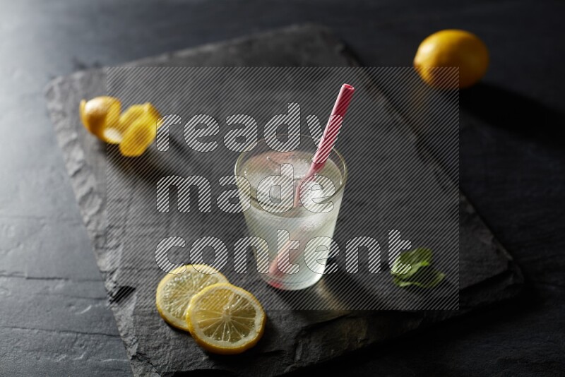 A glass of lemon juice with a straw on black background