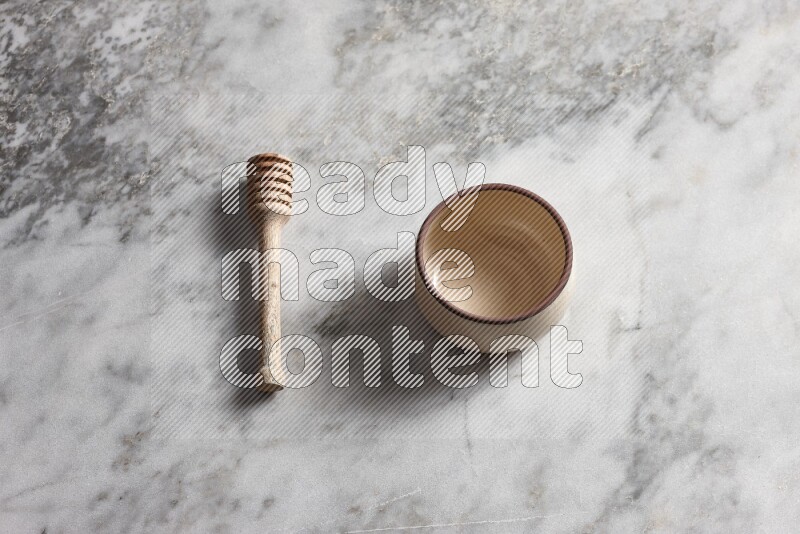 Beige pottery oven bowl with wooden honey dipper on the side on grey marble background