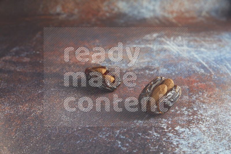 two almond stuffed madjoul dates on a rustic reddish background