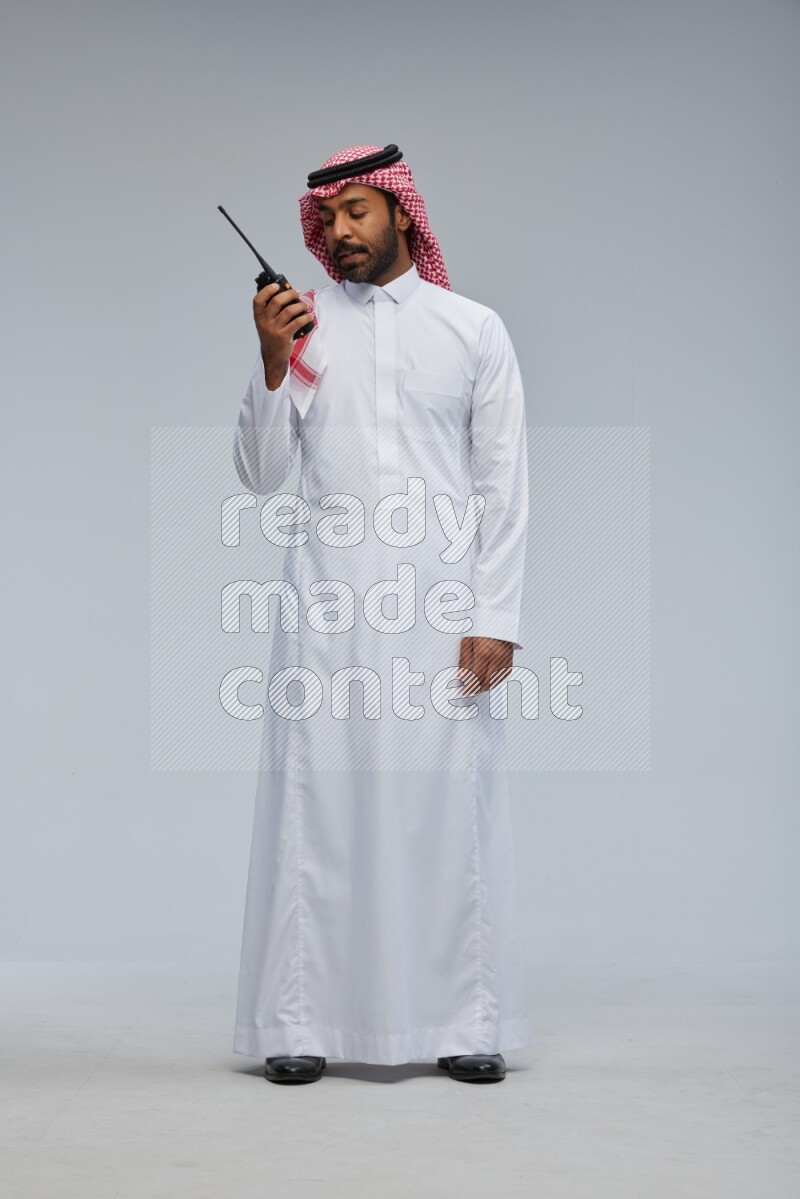 Saudi man Wearing Thob and shomag standing holding walkie-talkie on Gray background