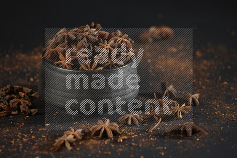 Star Anise in a black bowl with sprinkled anise on black flooring