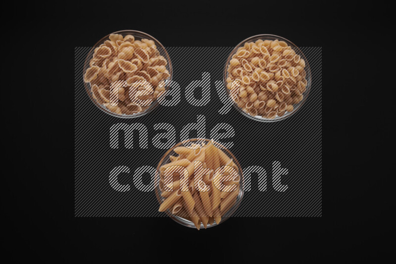 Different pasta types in glass bowls on black background