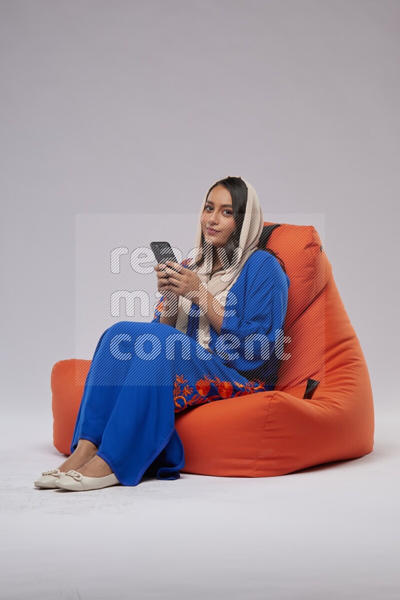 A Saudi woman sitting on an orange beanbag and texting on phone
