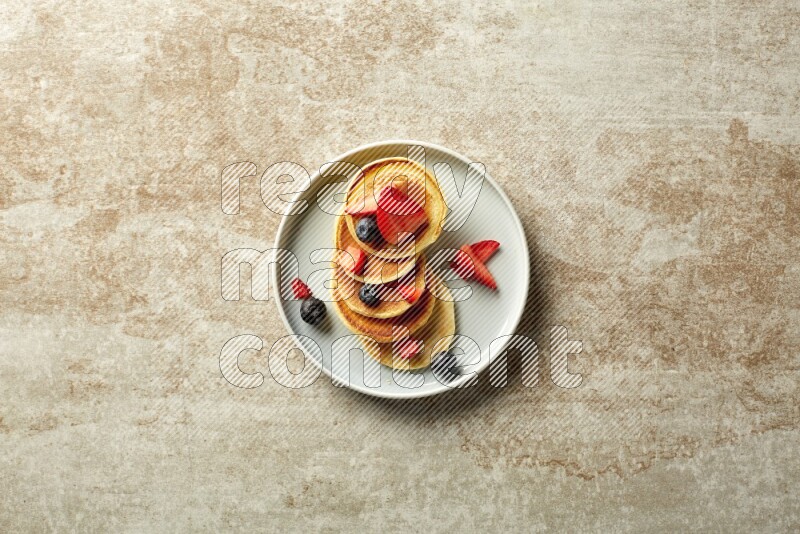 Five stacked mixed berries mini pancakes in a blue plate on beige background
