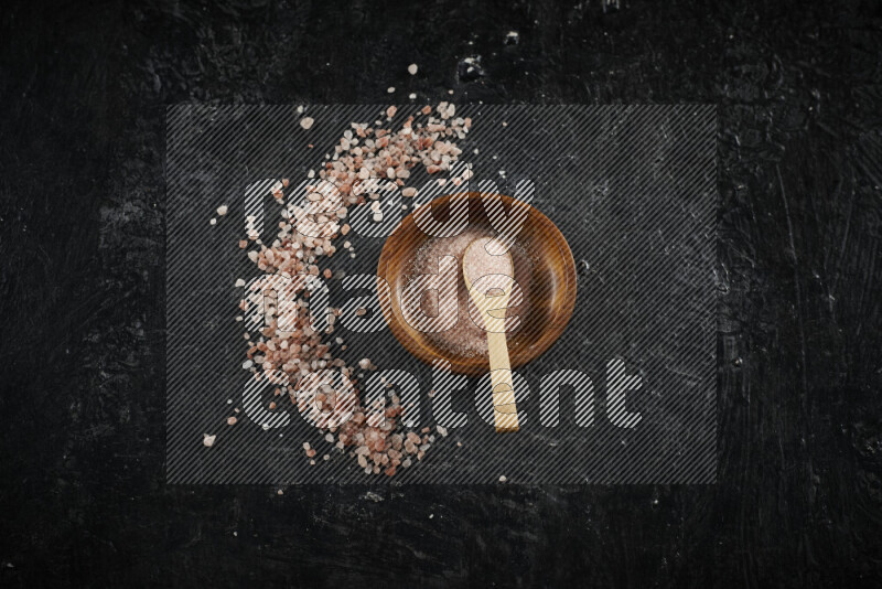 A pottery plate full of fine salt with bunch of coarse salt beside it on black background