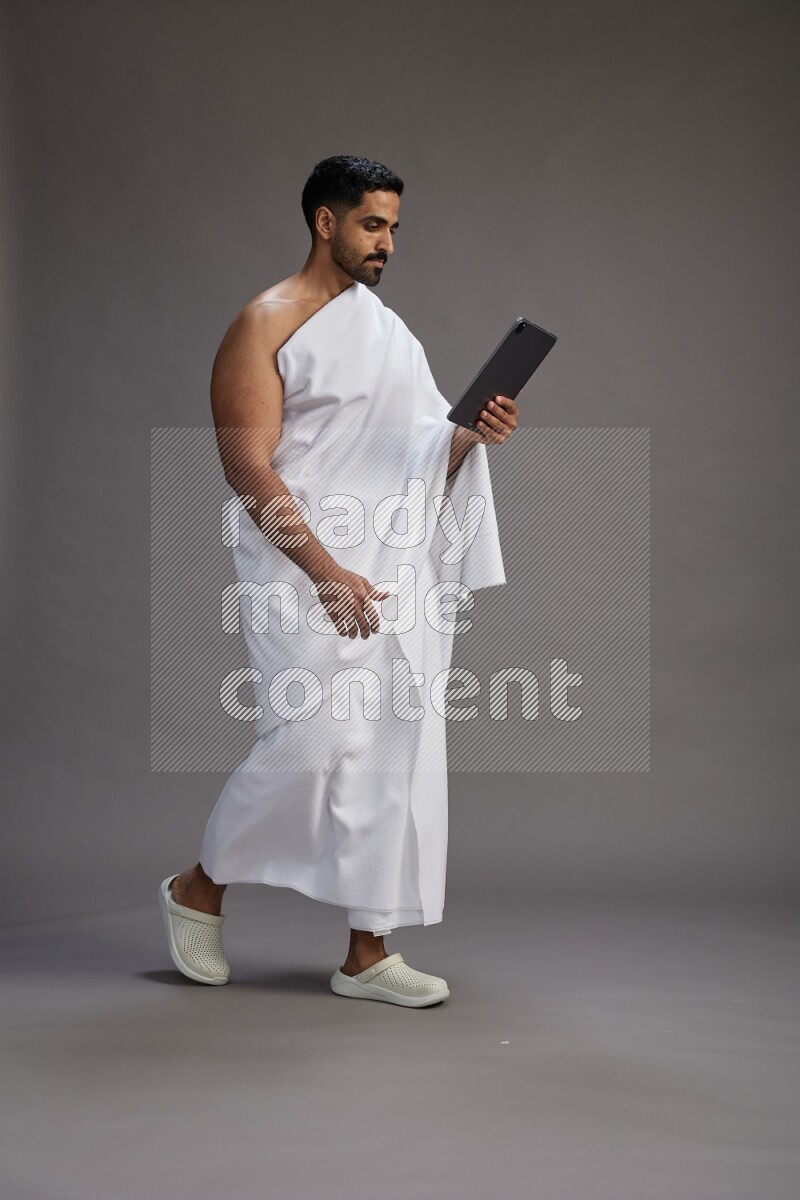 A man wearing Ehram and holding a tablet on gray background