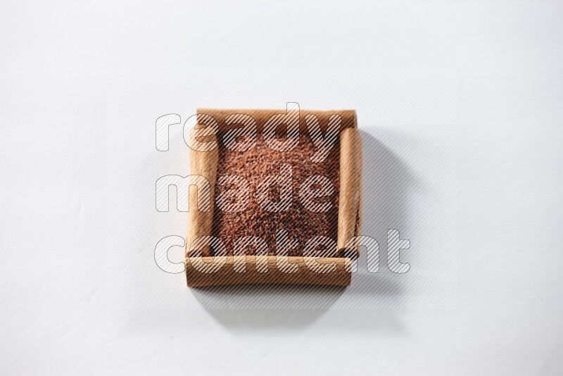 أربعة من أعواد القرفة مكونة شكل مربع بداخلها حب الرشاد علي خلفية بيضاء