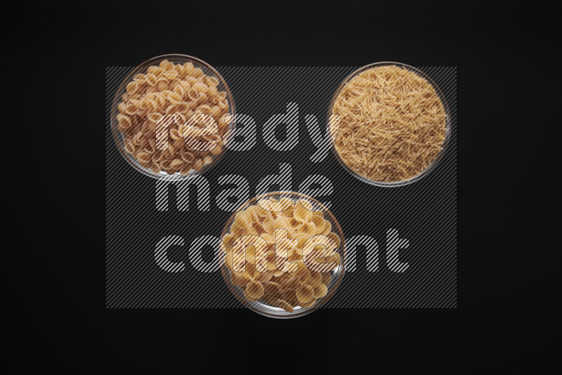Different pasta types in glass bowls on black background