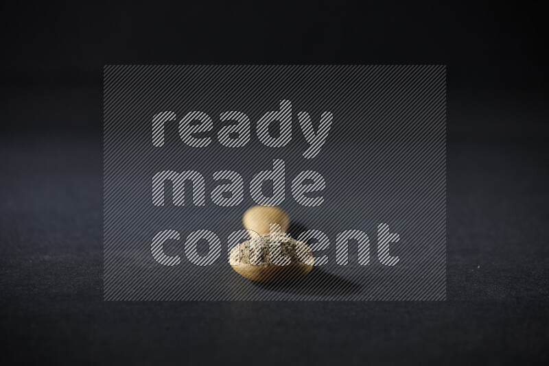 A wooden spoon full of cardamom powder on black flooring