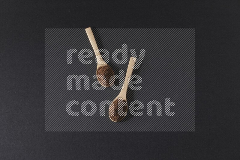 2 wooden spoons full of cloves powder on a black flooring