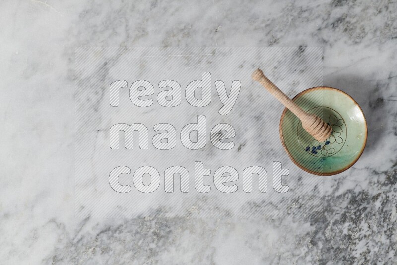 Decorative pottery plate with wooden honey dipper in it on grey marble background