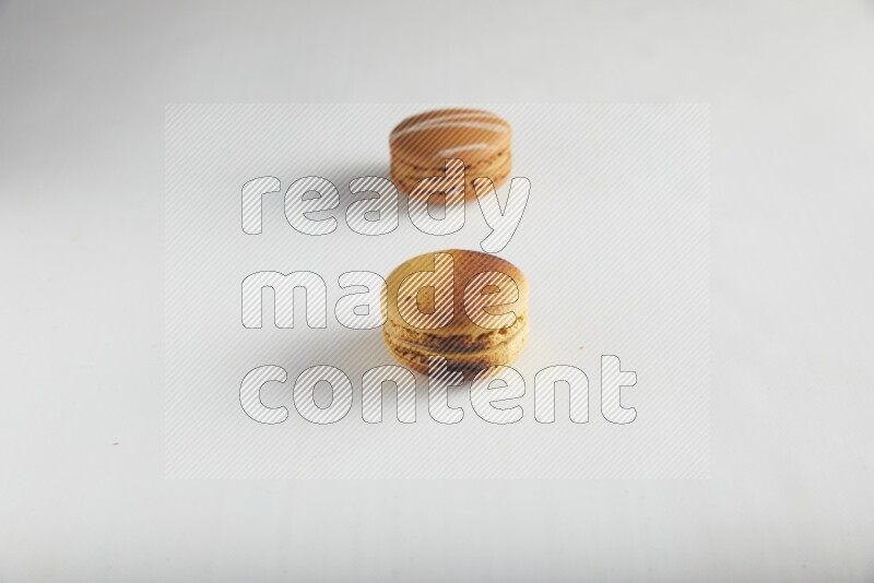 45º Shot of of two assorted Brown Irish Cream, and Yellow Crème Brulée macarons on white background