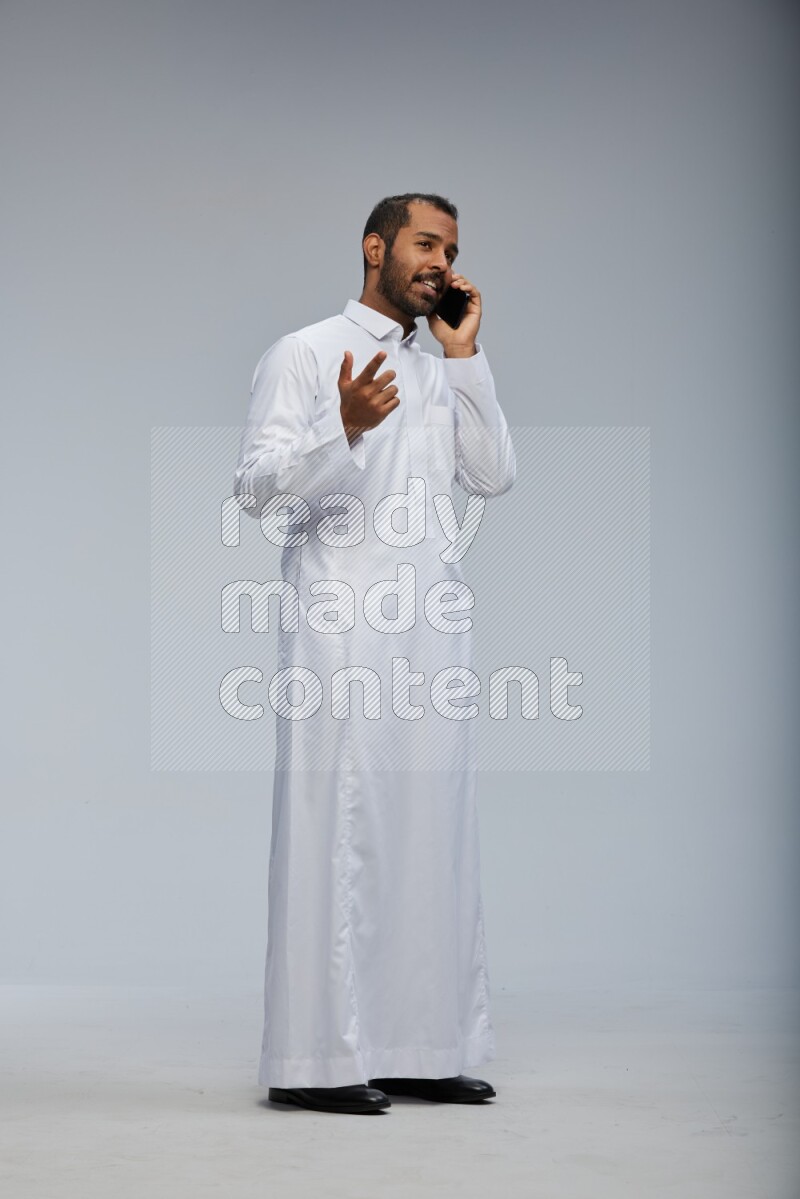 Saudi man wearing Thob standing talking on phone on Gray background