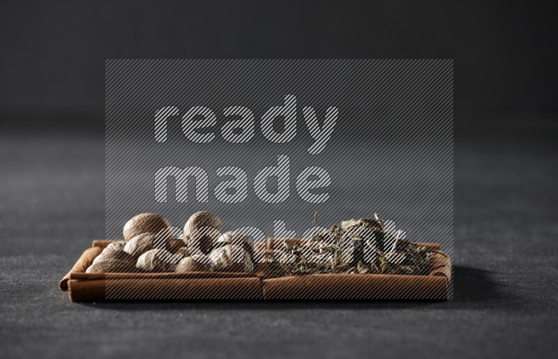 مربعان من أعواد القرفة ممتلئان بجوزة الطيب والريحان المجفف علي خلفية سوداء