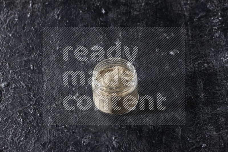 A glass jar full of white pepper powder on textured black flooring