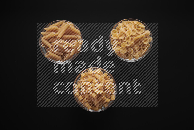 Different pasta types in glass bowls on black background