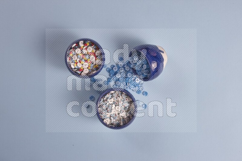 Multicolored pottery bowls full of colored buttons on blue background