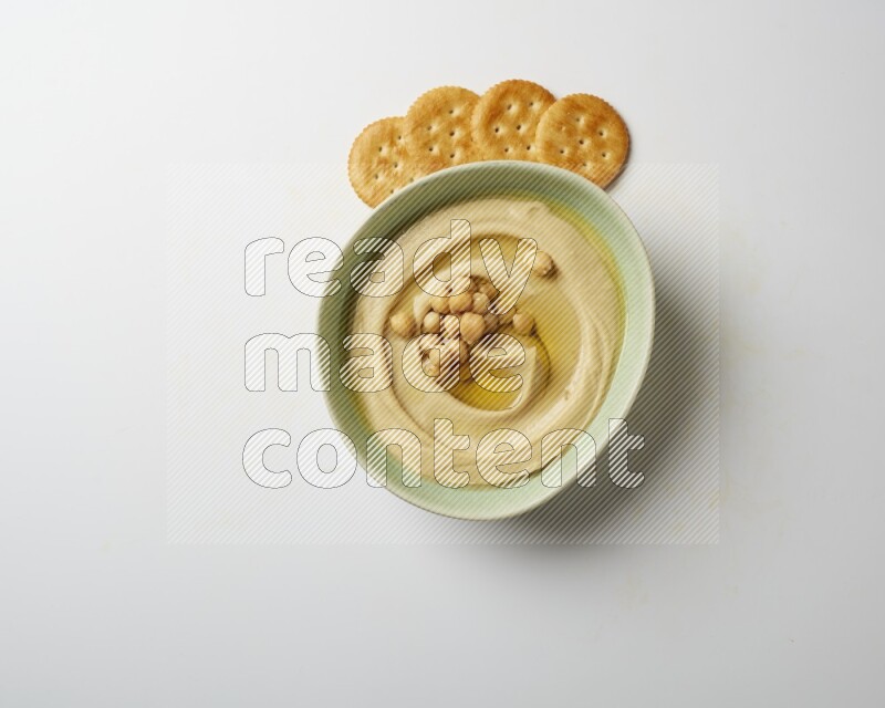 Hummus in a green plate garnished with roasted chickpeas  on a white background