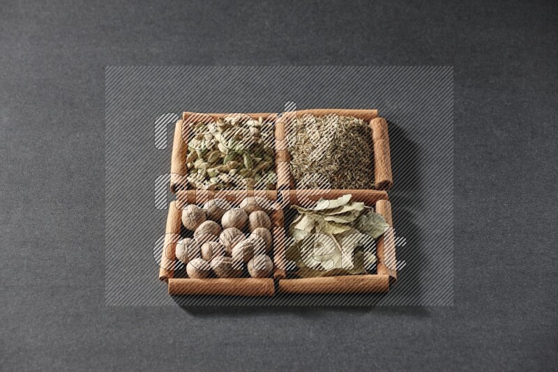 4 مربعات من عيدان القرفة ممتلئة بالكمون وحبوب الهيل وأوراق الغار وجوزة الطيب على أرضية سوداء