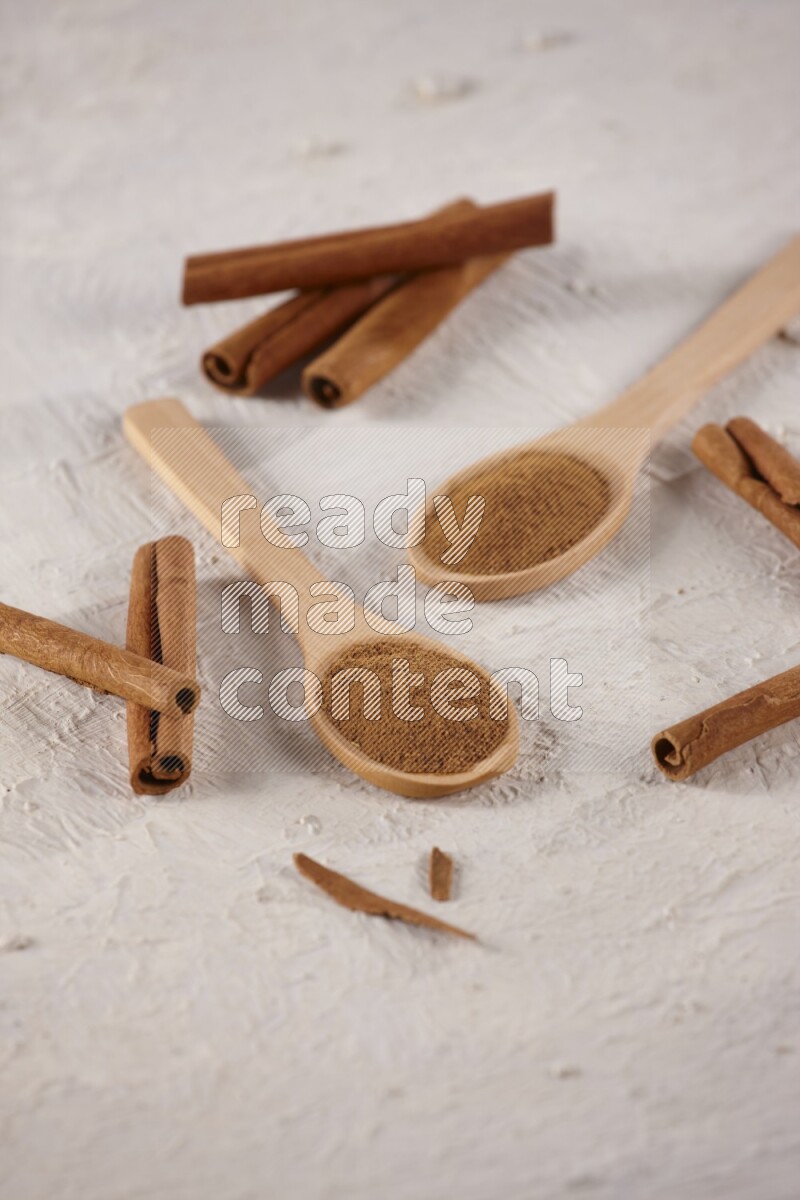 Two wooden spoons full of cinnamon powder with cinnamon sticks on white background
