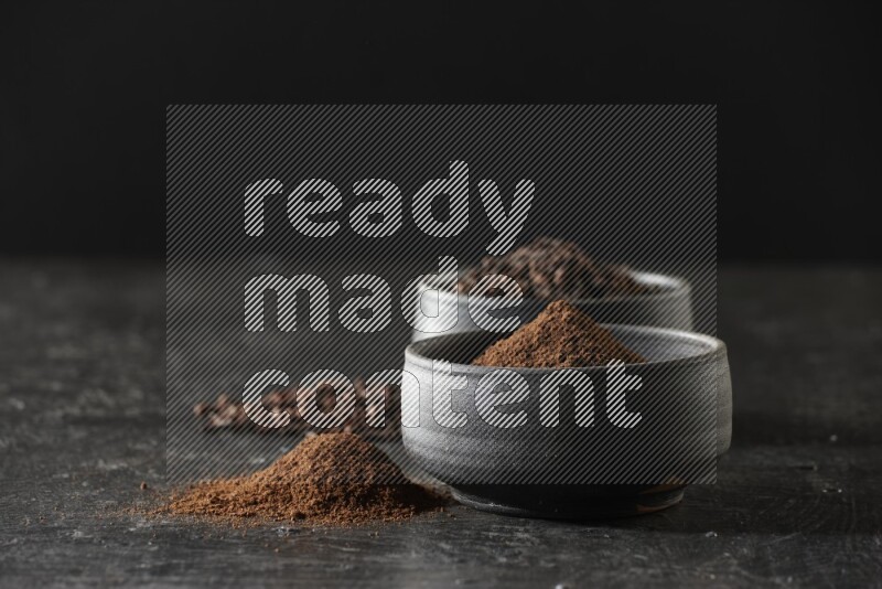 وعاءين من الفخار الأسود أحدهما ممتلئي بحبوب القرنفل والآخر ممتلئ ببودرة القرنفل على خلفية سوداء