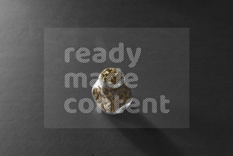 A glass spice jar full of cardamom on black flooring