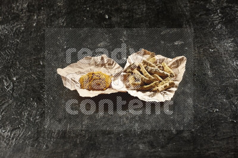 أصابع الكركم المجففة وبودرة الكركم في قطع من الورق على خلفية سوداء