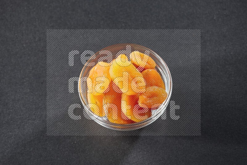 A glass bowl full of dried apricots on a black background in different angles