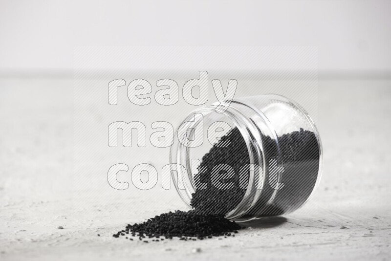A glass jar full of black seeds and the jar flipped and seeds spread on a textured white flooring