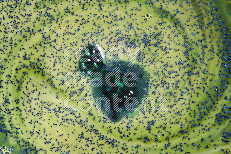 A close-up of sparkling blue glitter scattered on swirling blue and green background