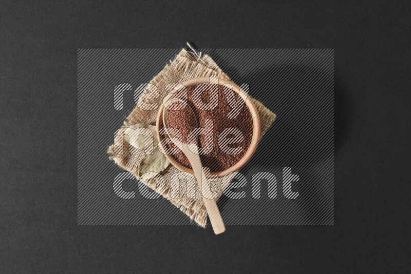 وعاء خشبي ممتلئ ببذور حب الرشاد وملعقة خشبية ممتلئة فوقه علي قطعة من القماش علي خلفية سوداء