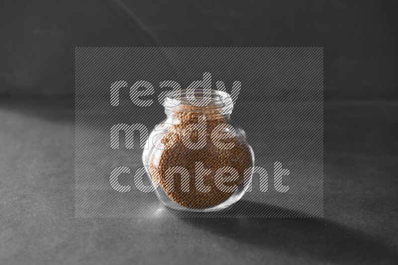 A glass spice jar full of mustard seeds on black flooring