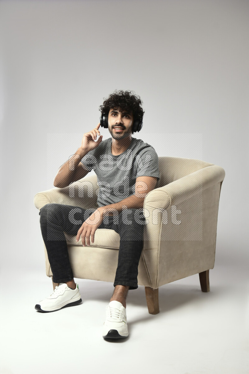 A man wearing casual sitting on a chair putting on headphones on white background