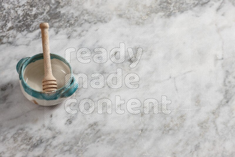 Multicolored pottery bowl with wooden honey dipper in it on grey marble background