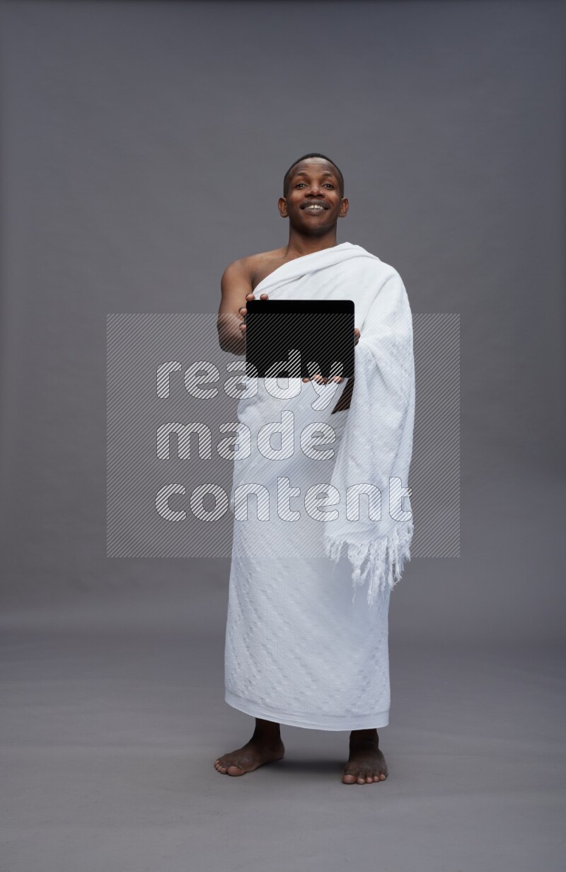 A man wearing Ehram Standing showing tablet to camera on gray background