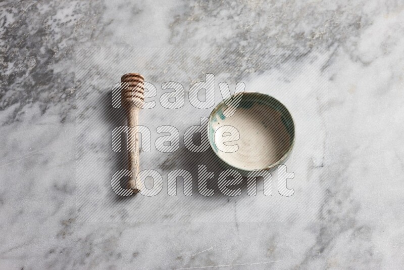 Multicolored pottery bowl with wooden honey dipper on the side on grey marble background