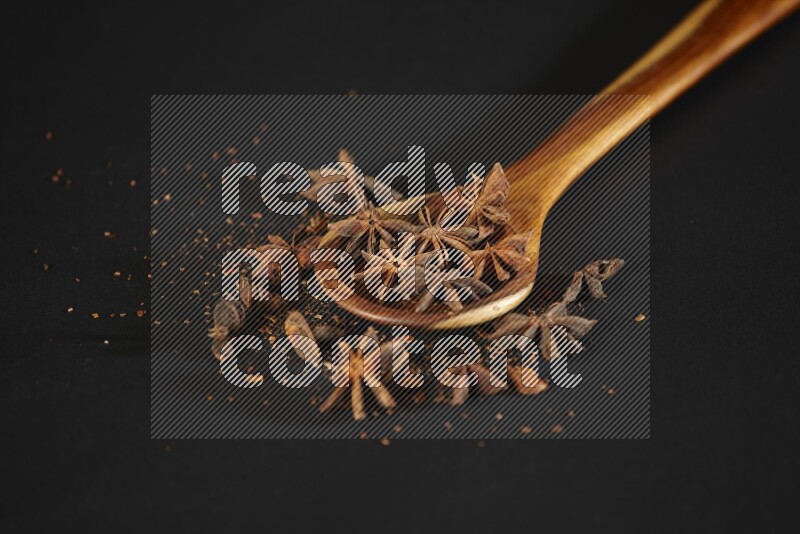 Star Anise in a wooden spoon ladle with more anise on black flooring