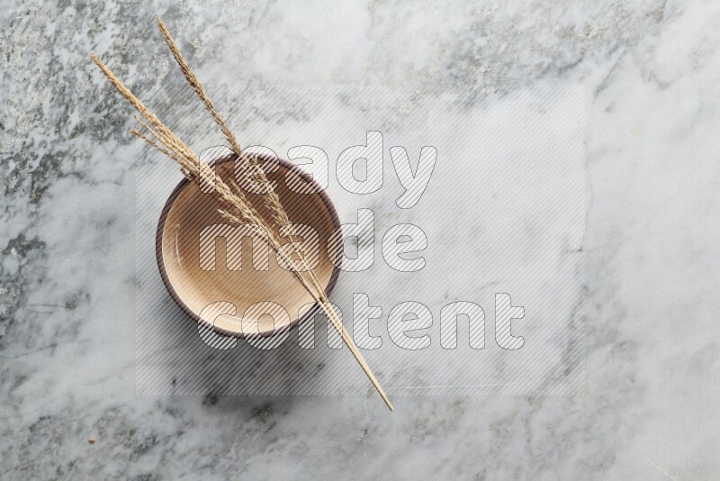 Wheat stalks on beige pottery oven bowl on grey marble background