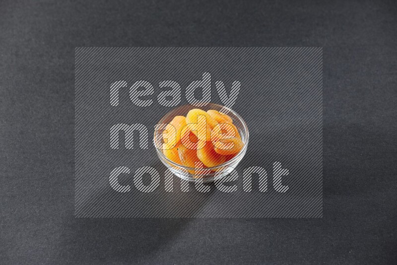 A glass bowl full of dried apricots on a black background in different angles