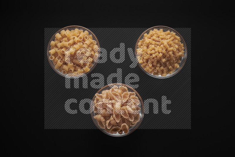 Different pasta types in glass bowls on black background