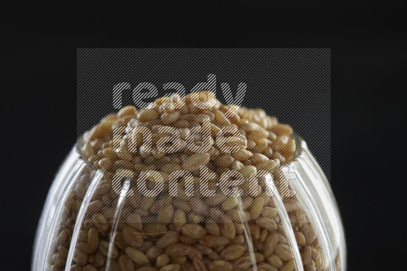 Hulled wheat in a glass jar on black background