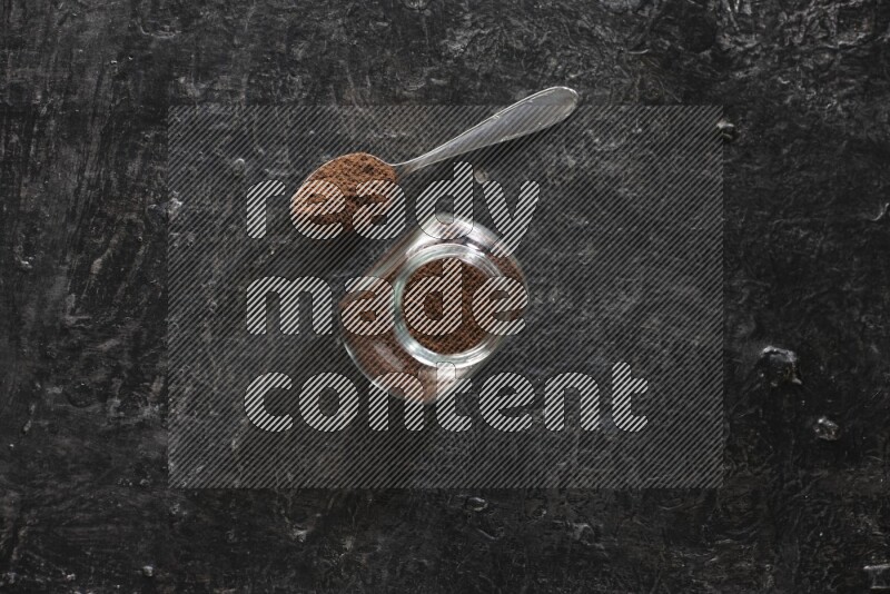 وعاء زجاجي للبهارات وملعقة معدنية ممتلئان ببودرة القرنفل على أرضية سوداء