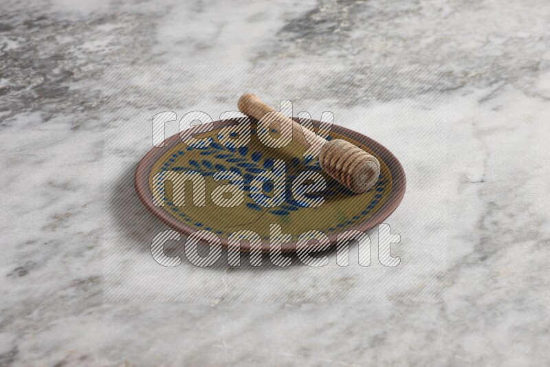 Decorative pottery plate with wooden honey dipper in it on grey marble background