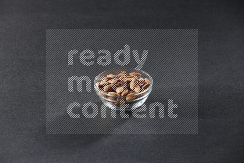 A glass bowl full of peeled almonds on a black background in different angles