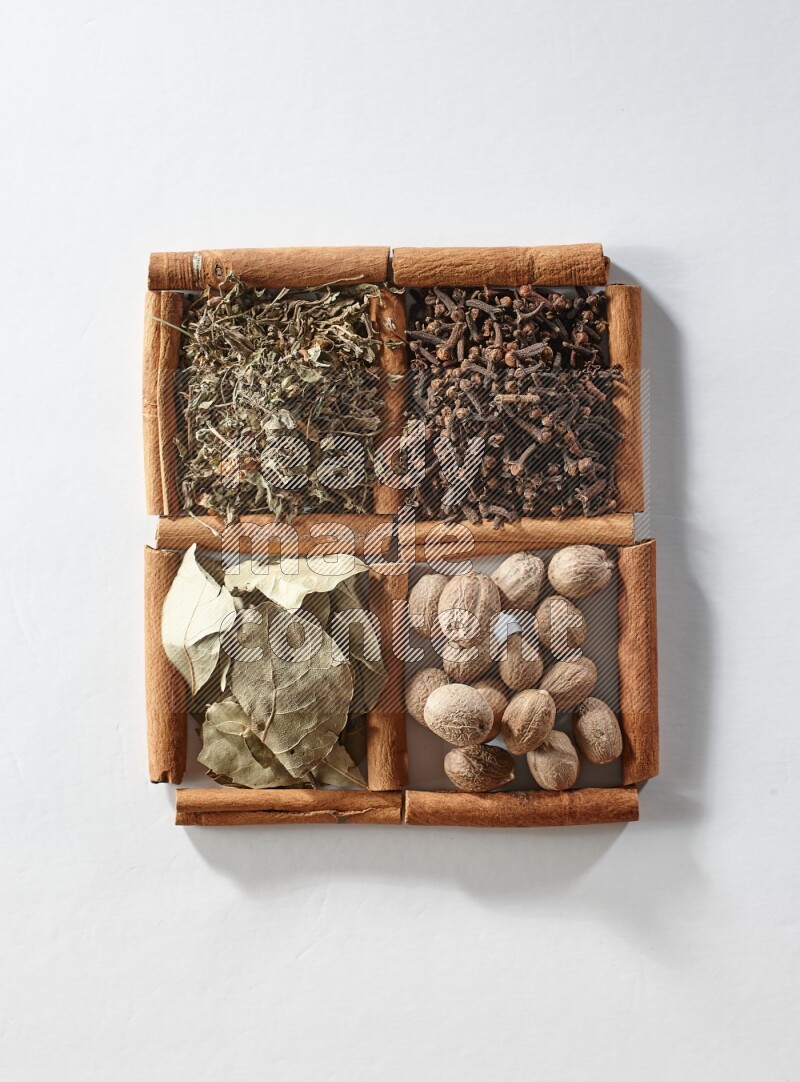 4 مربعات من أعواد القرفة ممتلئة بأوراق الغار والريحان المجفف والقرنفل وجوزة الطيب على أرضية بيضاء